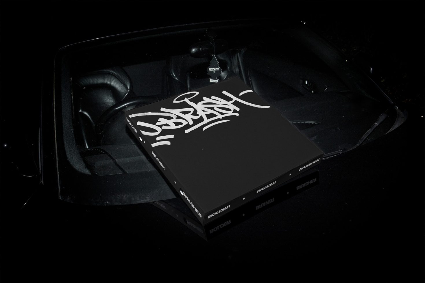 Laptop with graffiti-style logo on a car dashboard at night, reflecting modern graphic design and street art aesthetics for templates.